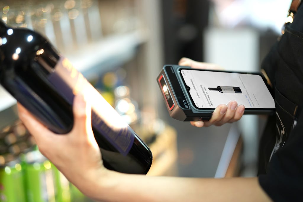 Close-up of a person scanning a wine bottle with a portable scanner in a store.